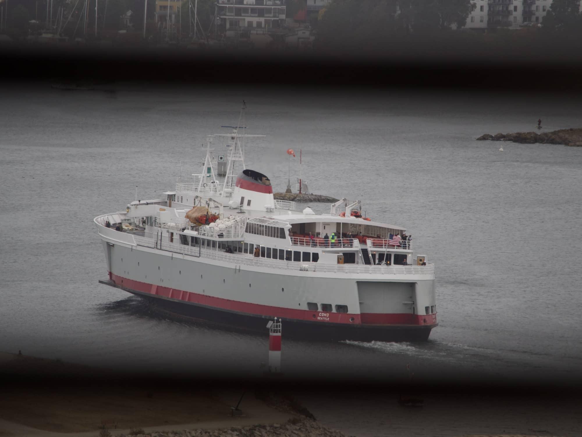 A white ferry with a red and black stripe turns to leave Victoria and head back to Seattle.